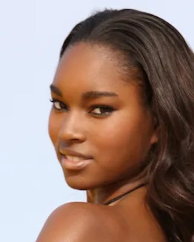 Damaris Lewis poses with her hair in a soft wave and smiles over her shoulder.